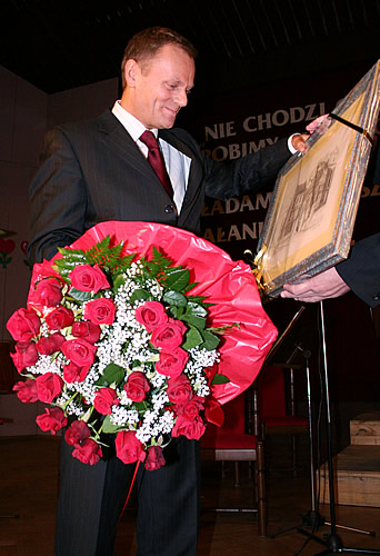 Donald Tusk z kwiatami i grafiką przedstawiającą Katedrę Łomzyńską