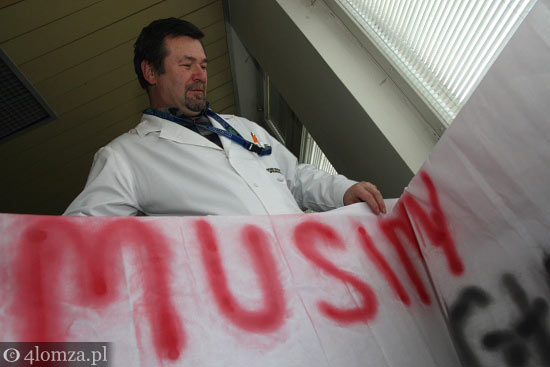 lekarz Andrzej Antosiuk zwija transparent z napisem
