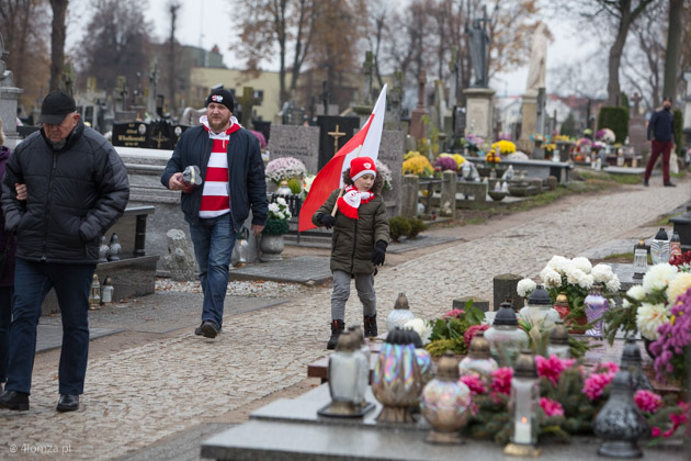Chłopiec z polską flagą i w szaliku ŁKSu maszeruje z tatą po cmentarzu