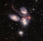 Foto: Kosmiczny Teleskop Jamesa Webba: Kwintet Stephana
Ogromna mozaika Kwintetu Stephana jest największym dotychczas obrazem z Kosmicznego Teleskopu Jamesa Webba, obejmującym około jednej piątej średnicy Księżyca. Zawiera ponad 150 milionów pikseli i składa się z prawie 1000 oddzielnych plików graficznych. Wizualne zgrupowanie pięciu galaktyk zostało uchwycone przez kamerę bliskiej podczerwieni Webba (NIRCam) i instrument średniej podczerwieni (MIRI). Dzięki swojemu potężnemu widzeniu w podczerwieni i niezwykle wysokiej rozdzielczości przestrzennej Webb pokazuje nigdy wcześniej nie widziane szczegóły w tej grupie galaktyk. Obraz ozdabiają lśniące gromady milionów młodych gwiazd i obszary rozbłysku gwiazd narodzin świeżych gwiazd. Zamiatające ogony gazu, pyłu i gwiazd są ściągane z kilku galaktyk z powodu oddziaływań grawitacyjnych. Najbardziej dramatycznie, instrument MIRI Webba rejestruje ogromne fale uderzeniowe jako jedna z galaktyk, NGC 7318B, rozbija się przez klaster.