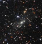 Foto: Pierwsze zdjęcie teleskopu  Jamesa Webba
Tysiące galaktyk zalewa to zdjęcie gromady galaktyk SMACS 0723 w bliskiej podczerwieni. Obrazowanie w wysokiej rozdzielczości z Kosmicznego Teleskopu Jamesa Webba w połączeniu z naturalnym efektem znanym jako soczewkowanie grawitacyjne umożliwiło wykonanie bardzo szczegółowego zdjęcia. Najpierw skup się na galaktykach odpowiedzialnych za soczewkowanie: jasnej białej galaktyce eliptycznej w centrum obrazu i mniejszych białych galaktykach na całym zdjęciu. Związane grawitacyjnie w gromadzie galaktyk, uginają światło z galaktyk, które pojawiają się w ogromnych odległościach za nimi. Połączona masa galaktyk i ciemnej materii działa jak kosmiczny teleskop, tworząc powiększone, powykrzywiane, a czasem lustrzane obrazy poszczególnych galaktyk. Wyraźne przykłady odbicia lustrzanego znajdują się w widocznych pomarańczowych łukach na lewo i prawo od najjaśniejszej galaktyki gromady. (źródło: NASA)