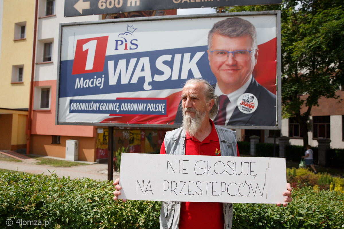 Pan Witold przed banerem Macieja Wąsika z tabliczką 